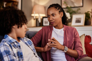 Black mother on couch sitting next to teenage son looking at each other